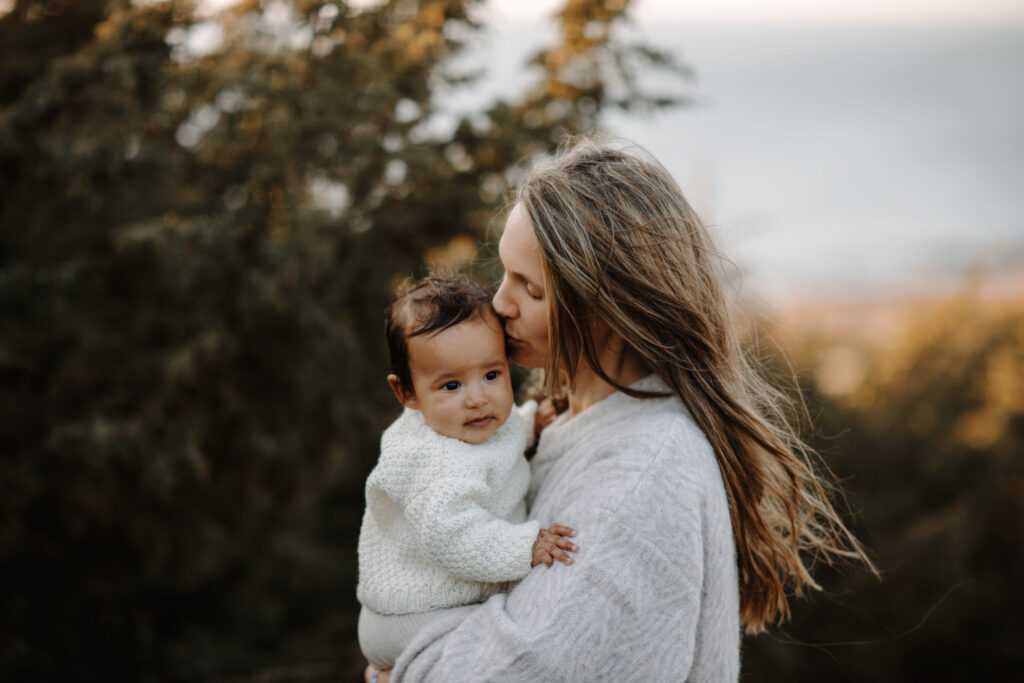 Mamma håller sitt barn i famnen under en moderskapsfotografering i skogsmiljö nära Göteborg